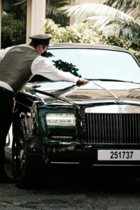 A suited man cleaning the windshield of a Rolls-Royce, symbolizing understated luxury and attention to detail.