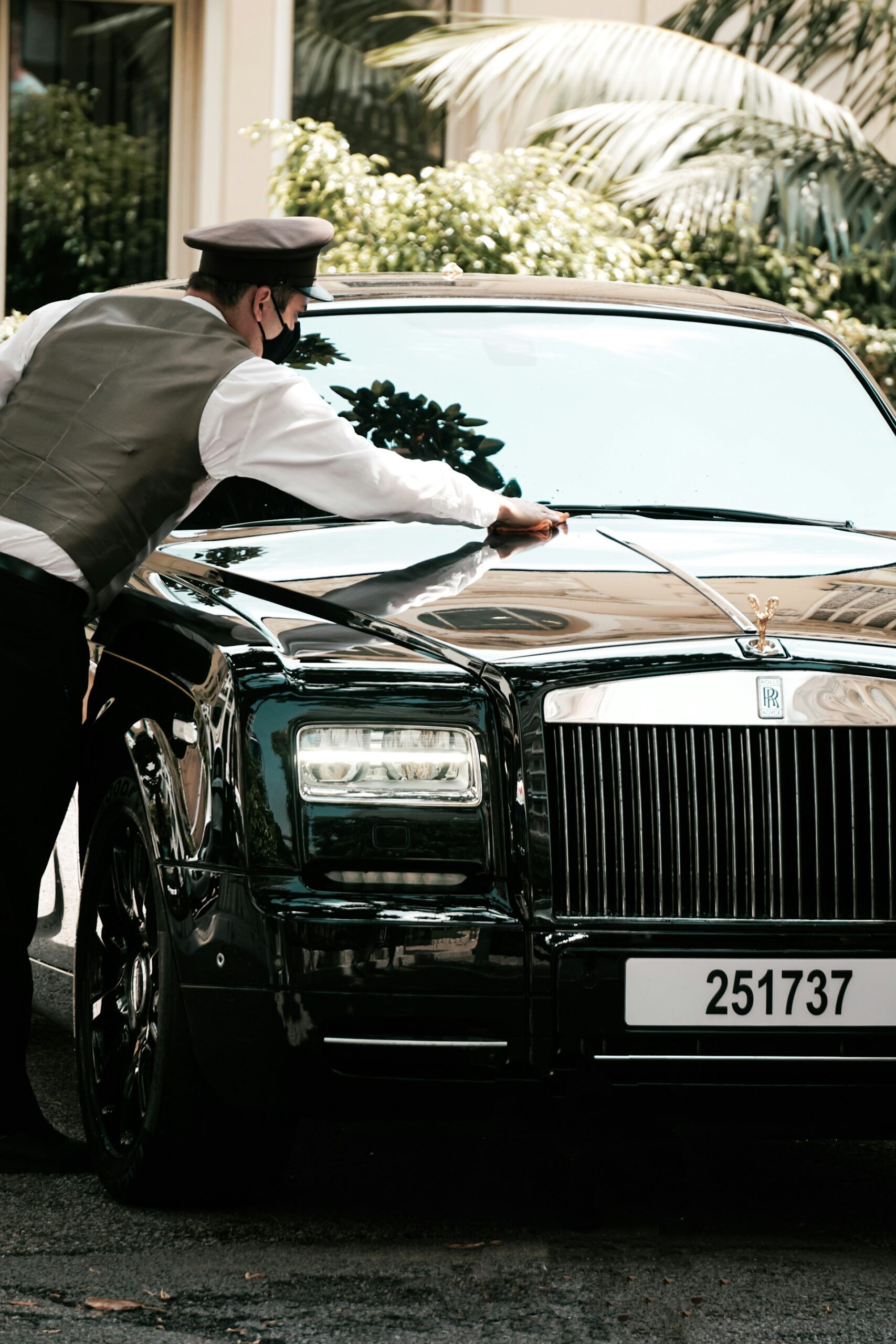 A suited man cleaning the windshield of a Rolls-Royce, symbolizing understated luxury and attention to detail.