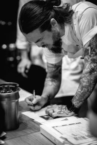 chef with tattoo plating fine dining dish in modern professional kitchen